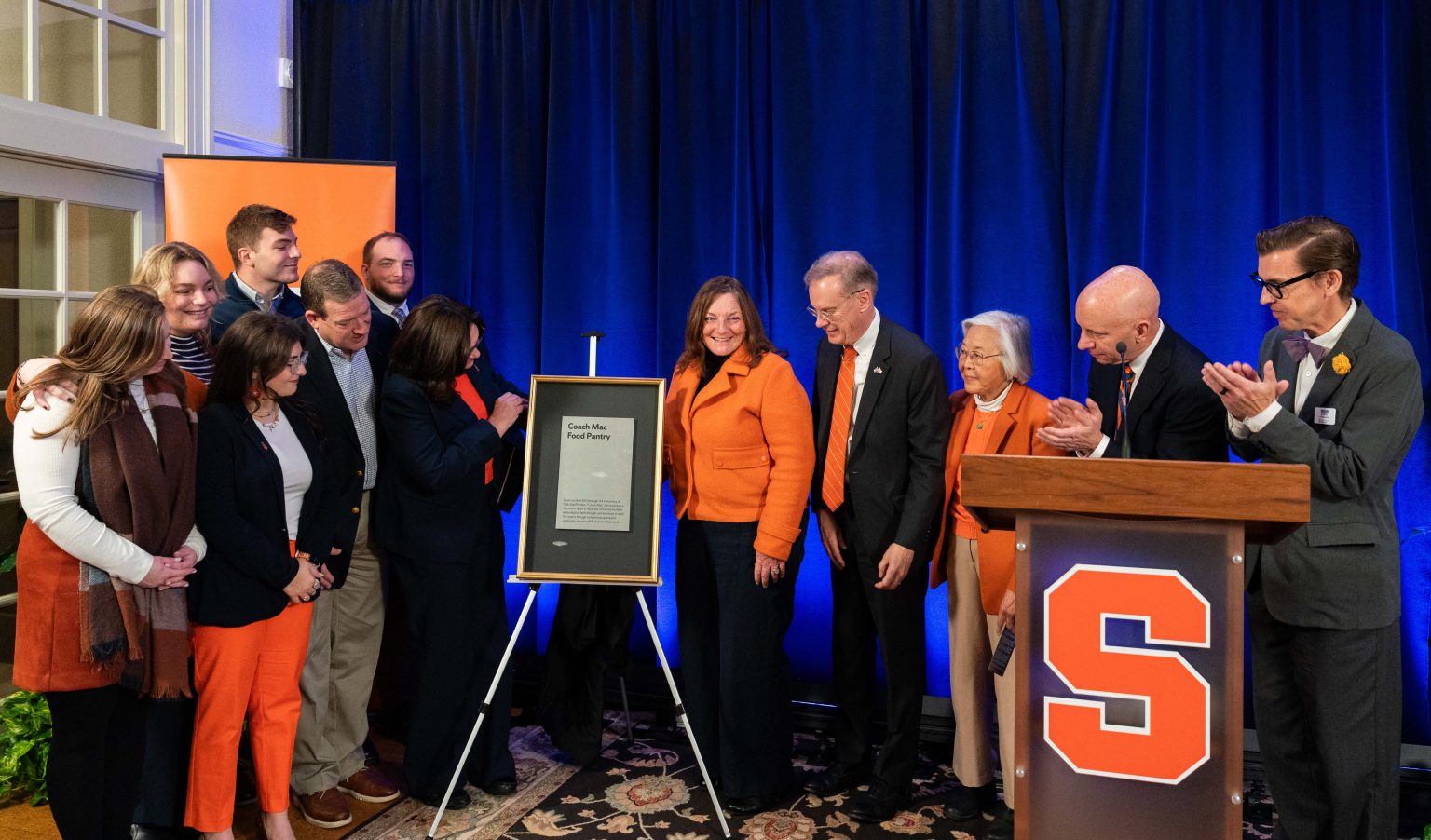 Event participants on stage in front of plaque